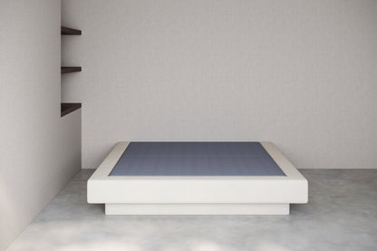 Minimalist white platform bed with anti slip base against a plain wall.